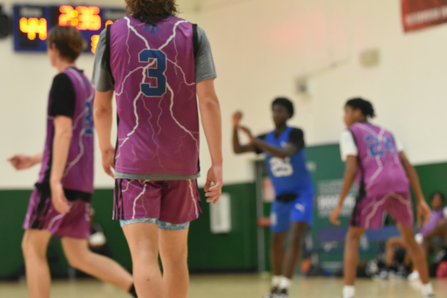 Basketball players in purple and black jerseys on an indoor court.